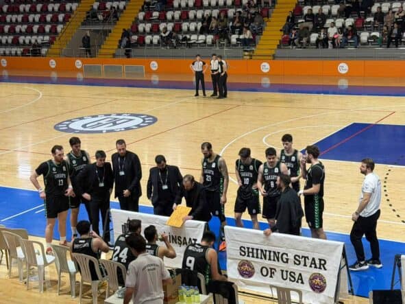 Antrenman ve maç hazırlıkları yapan basketbol ekibi, seyircilerle dolu salonda sahaya odaklanmış durumda.