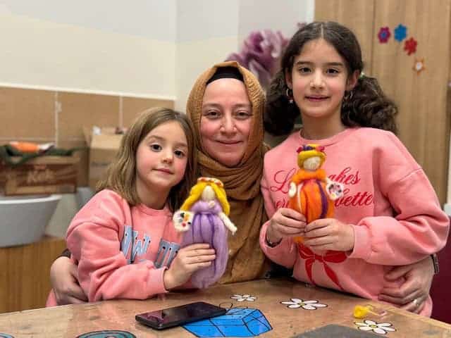 Sevimli çocuklar ve öğretmen, el sanatlarıyla hazırlanan oyuncak bebekleri gösteriyor.