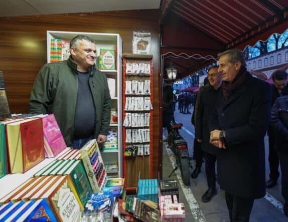 İnsanlar kitap standında sohbet ederken, basın merkezi etkinliği ve kitap tanıtımı.